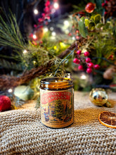 Load image into Gallery viewer, Spiced Orange Candle in a clear glass jar with a vintage red and gold Christmas tree label and lit wick