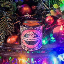 Load image into Gallery viewer, Apple and Cinnamon vintage vegan candle with festive Victorian label surrounded by Christmas decorations and colorful lights