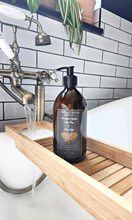 Load image into Gallery viewer, 500ml amber glass bottle of vintage vegan body and hand wash with lemongrass and ginger scent placed on a wooden bath tray by a bathtub and running faucet