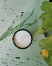 Load image into Gallery viewer, Tibetan Cedarwood & Jasmine soy wax candle lit on rustic green surface with lavender sprigs and green leaves nearby