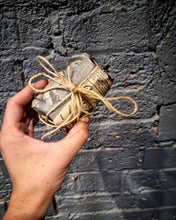 Load image into Gallery viewer, Hand holding Australia Peppermint and Eucalyptus soy wax candle wrapped in vintage newspaper with twine against textured gray wall background