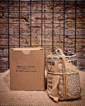 Load image into Gallery viewer, South London Collection vintage vegan candle wrapped in newspaper print and tied with twine next to a brown cardboard box against a brick wall background