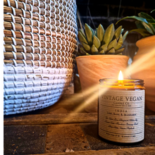 Load image into Gallery viewer, India Lime Basil & Mandarin soy wax candle lit next to wicker basket and potted succulent plant on wooden surface